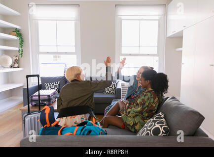 Junge Frauen Freunde mit Koffer high-fiving im Wohnzimmer Stockfoto