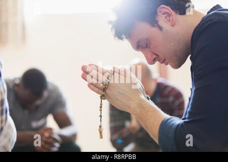 Ruhige Mann, der betet mit Rosenkranz in der Gebetsgruppe Stockfoto