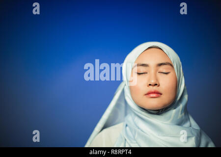 Ruhige junge Frau trägt blaue Seide hijab Stockfoto