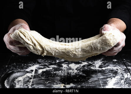 Cook erstreckt sich knetete Teig aus weissem Mehl von Weizen über einen schwarzen Holztisch Stockfoto