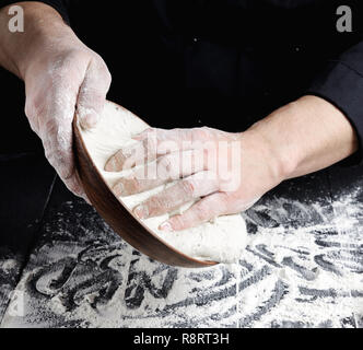 Hände kneten von man Weißes Weizenmehl Teig auf schwarzem Hintergrund Holz, in der Nähe Stockfoto