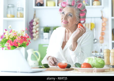 Ältere Frau in Haar rollen Schneiden von Gemüse auf Küche Stockfoto
