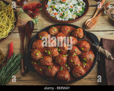 Hausgemachte Frikadellen in Tomatensoße. Pfanne auf einer hölzernen Oberfläche, Reis mit Gemüse, Pasta Stockfoto
