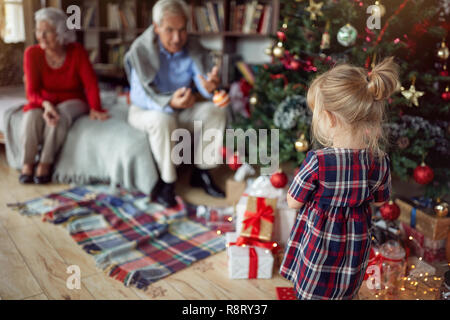 Süße Mädchen spielt vor einem geschmückten Weihnachtsbaum Stockfoto