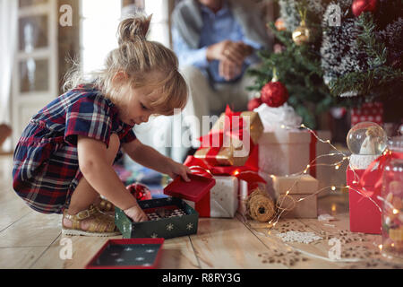 Süße kleine Mädchen spielt vor einem geschmückten Weihnachtsbaum Stockfoto