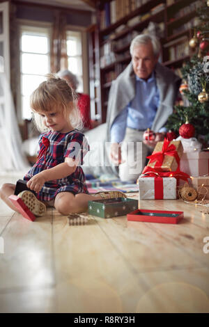 Nettes Mädchen ist offen Weihnachtsgeschenk vor einem eingerichteten X-mas Tree Stockfoto
