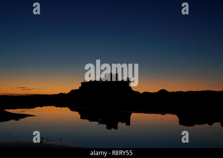 Die Sonne geht hinter Bamburgh Castle in Northumberland, an der Nordostküste von England nach einem Wochenende die Temperaturen in einigen Teilen des Vereinigten Königreichs dip unter dem Gefrierpunkt. Stockfoto