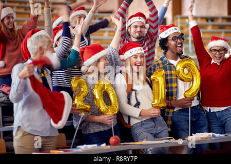 Gerne Studenten in Santa Hut Holding 2019 goldene Luftballons am Neuen Jahr Partei auf Universität Stockfoto