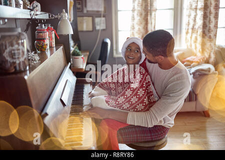 Glückliche junge Vater mit Kind Mädchen auf Weihnachten Musik am Piano. Stockfoto