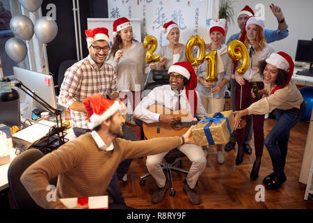 Lächelnd business Arbeiter haben Spaß in Santa hat bei der Weihnachtsfeier und Geschenke auszutauschen im Büro Stockfoto