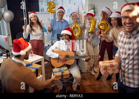 Lächelnd Geschäft Leute Spaß haben und tanzen in Santa Hut auf Xmas Party und zum Austausch der Geschenke im Büro Stockfoto