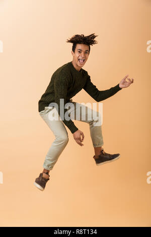 Volle Länge Foto von fröhlichen african american Guy tragen Pullover lachen und springen über beigen Hintergrund isoliert Stockfoto