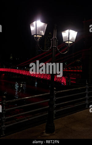 Klassische Straßenlaternen vor dem cavenaugh Brücke, die einzige Hängebrücke auf dem Singapore River, in Rot in der Nacht beleuchtet. Stockfoto