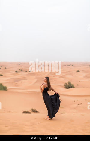 Junge Frau im schwarzen Kleid steht auf Düne in Wüste am sonnigen, heissen Tag Stockfoto