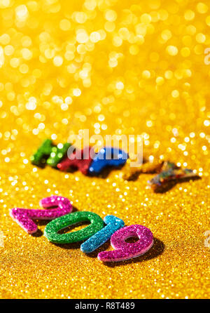 Nahaufnahme von einigen glitter Buchstaben und Zahlen in verschiedenen Farben, die den Text gerne 2019, auf eine helle glitzernde gelber Hintergrund mit einigen leeren Stockfoto