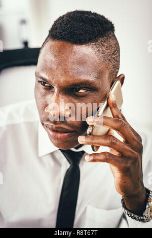 Das Porträt einer nachdenklich Afrikanischen Geschäftsmann, der sich auf dem Smartphone im modernen Büro. Stockfoto