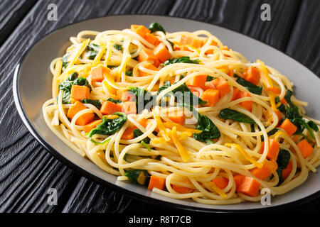 Bio Spaghetti essen mit Kürbis, Spinat und Cheddar Käse close-up auf einem Teller auf den Tisch. Horizontale Stockfoto