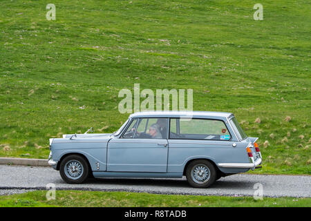 Ältere Paare fahren 1967 classic car Triumph Herald 1200 Immobilien entlang der Landstraße durch Wiese Stockfoto