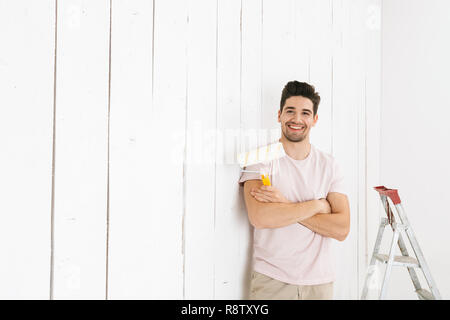 Bild der männlichen Mann 20 s Malerei weiße Wand und mit Paint roller Renovierung Stockfoto