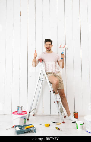 Volle Länge Foto von brunette Kerl 20 s auf Leiter und Malerei Wand während der Sanierung stehen Stockfoto