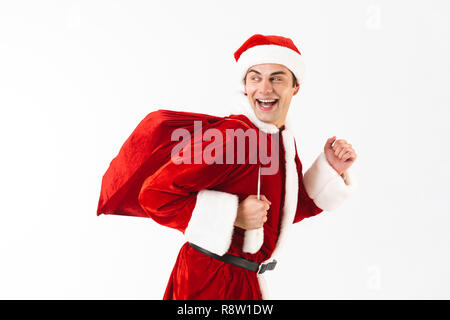 Portrait von freudiger Mann 30 s in santa claus Kostüm und Red Hat mit Geschenk Tasche über der Schulter auf weißem Hintergrund im Studio isoliert Stockfoto