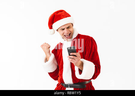 Bild von positiver Mann 30 s in santa claus Kostüm holding Smartphone auf weißem Hintergrund im Studio isoliert Stockfoto
