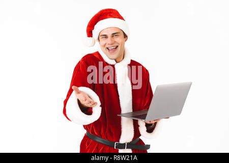 Porträt einer fröhlicher junger Mann in santa claus Kostüm auf weißem Hintergrund gekleidet, Laptop Stockfoto