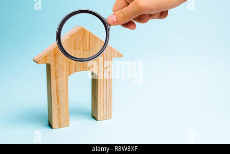 Lupe betrachtet das Holzhaus auf einem blauen Hintergrund. Die Kreditvergabe an die Öffentlichkeit. Das Konzept der erschwinglichen Wohnraum und Hypotheken eine zu kaufen Stockfoto