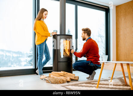 Junges Paar in hellen Pullover aufwärmen in der Nähe der Feuerstelle im modernen Haus in den Bergen im Winter gekleidet Stockfoto