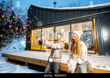 Junge glückliches Paar in Pullover feiern Winterurlaub vor einem wunderschönen eingerichteten Haus in den Bergen angezogen Stockfoto