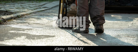 Low Angle View des Arbeitnehmers mit rüttelplatte bis zu beenden, das Patchen eines Stoß in der Straße mit frischem Asphalt. Breite Bild anzeigen. Stockfoto