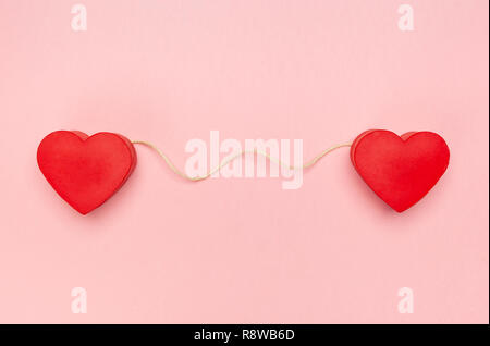 Paar rote Herzen mit einer Zeichenkette von Garn auf rosa Hintergrund verbunden. Stockfoto