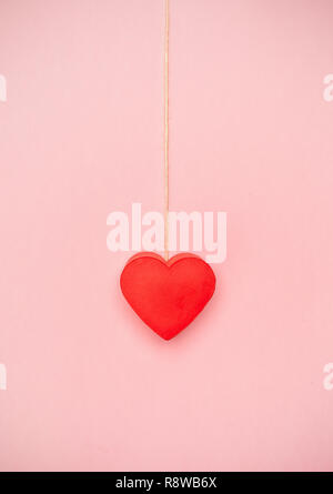 Herz hängt an einer Schnur von Garn auf rosa Hintergrund. Liebe Konzept an einem seidenen Faden hängen. Stockfoto