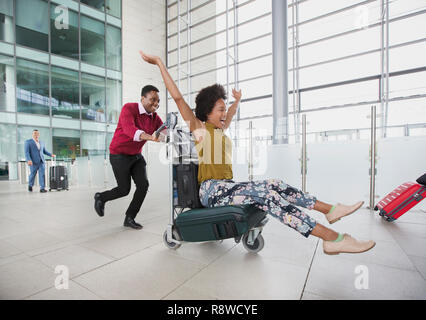 Verspieltes Paar, dass mit Gepäckwagen in Flughafen Stockfoto