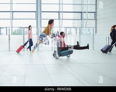 Verspieltes Paar drücken Gepäckwagen in Flughafen Stockfoto