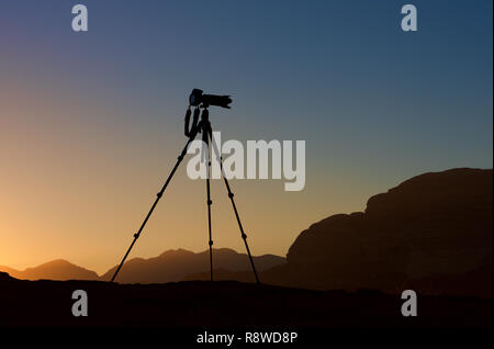 Kamera auf einem Stativ im Sonnenaufgang Hintergrund isoliert. Silhouette der Kamera auf Stativ mit Bergen im Hintergrund im Sonnenaufgang, Kamera bereit Fotos zu nehmen Stockfoto