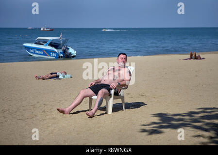 Mann, Sonnenbaden am Strand, saß auf einem Stuhl aus Kunststoff Stockfoto