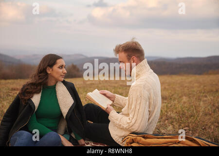 Zwei Jugendliche, 20-29 Jahre alt, Paare oder Freunde, sitzen auf den Berg Feld draußen, entspannen, ein Buch lesen, Mann, Frau, zuhören. Stockfoto