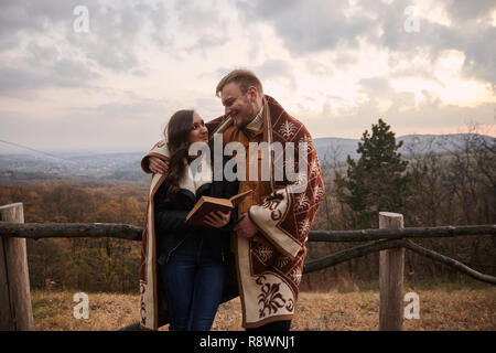 Zwei junge Leute, Paar, ein Buch lesen, im Freien in der Natur, an einander suchen, von Angesicht zu Angesicht. Herbst Kleidung, unter einer Decke. Stockfoto