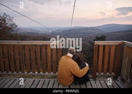 Zwei junge Leute, Paar, umarmen, sitzen an Deck, mit Blick auf die schöne Landschaft mit Landschaft Berge und den Sonnenuntergang Himmel im Freien, im Nationalen Stockfoto