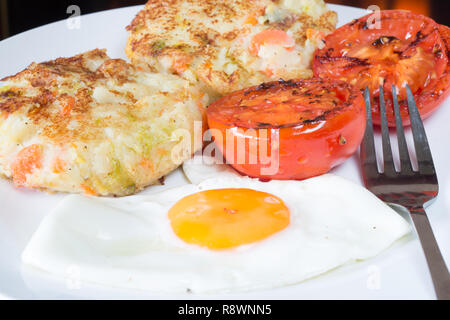 Ein traditionelles Gericht der übrig gebliebene Weihnachtsessen veg in Bubble und Squeak mit Spiegelei serviert und gegrillten Tomaten Stockfoto