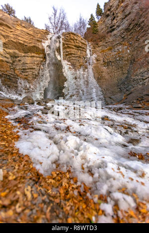 Teilweise gefrorenen Wasserfall mit Blätter auf dem Boden Stockfoto