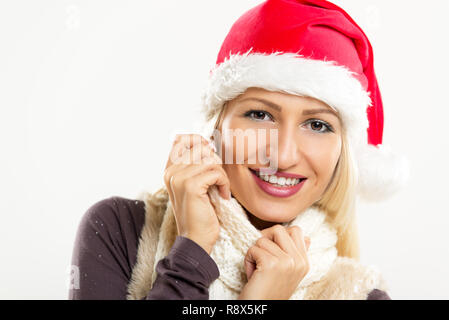 Eine junge hübsche blonde Mädchen mit Santa's Hut auf den Kopf und lächelte, sieht in die Kamera und stopfte es in ihr Schal. Stockfoto