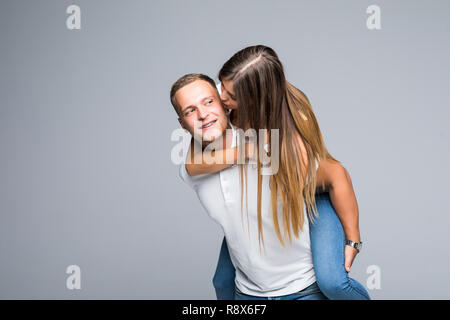 Junge brunete gutaussehenden Freund ist piggy Backing seine niedlichen Liebhaber, legere Kleidung, auf grauem Hintergrund Stockfoto