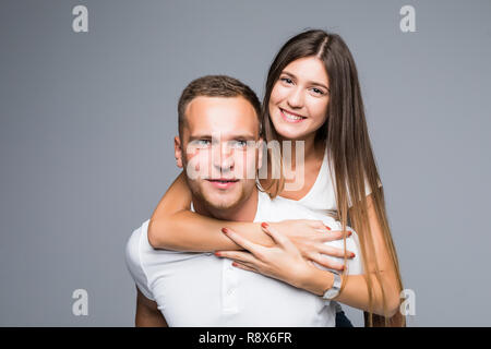 Junge brunete gutaussehenden Freund ist piggy Backing seine niedlichen Liebhaber, legere Kleidung, auf grauem Hintergrund Stockfoto