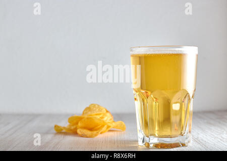 Ein Glas kaltes, Weizen, helles Bier mit Chips auf dem Tisch verstreut. kopieren. Stockfoto