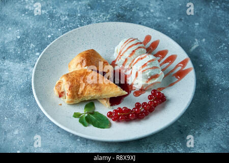 In Scheiben geschnittene Hausgemachte berry Strudel mit frischen rote Johannisbeere Beeren und Puderzucker auf einem alten Hintergrund serviert auf einem Teller mit Eis Stockfoto