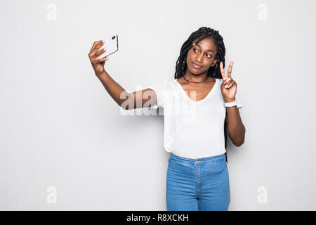 Junge lustig afrikanischen Casual lady Grimassen und selfie auf dem Smartphone über Grau isoliert Stockfoto