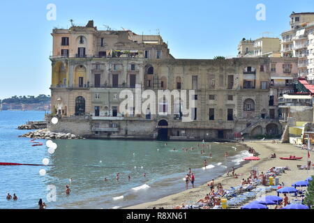 Sandstrand mit Badenden und Sonnenschirme auf der mediterranen Küste direkt neben und unter historischen und Mehrfamilienhäusern. Stockfoto