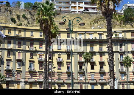 Traditionelle mediterrane Apartment Gebäude mit hohen Decken und einen kleinen Balkon mit felsigen Klippe hinter und hohen Palmen. Stockfoto